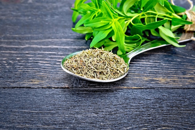 Savory dry in a metal spoon a bunch of fresh herbs on a background of wooden board