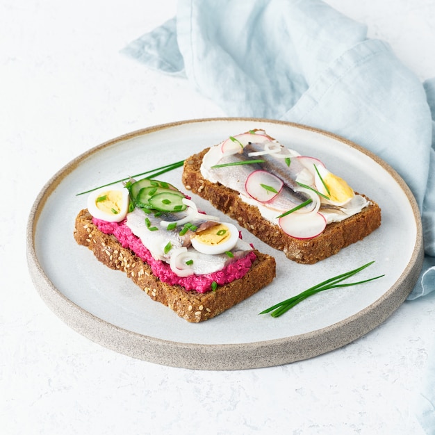 Savory smorrebrod, two traditional Danish sandwiches. Black rye bread with anchovy,