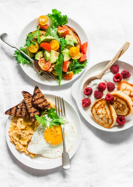 Savory and sweet breakfast avocado cherry tomatoes grilled bread salad fried egg with hummus and rye croutons and pancakes with greek yogurt and raspberries