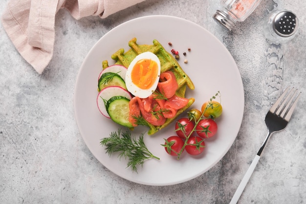 Savory waffles Breakfast green waffles wild garlic or spinach with egg tomato salmon on plate for breakfast on grey concrete table background Light dinner lunch or breakfast Top view Mock up