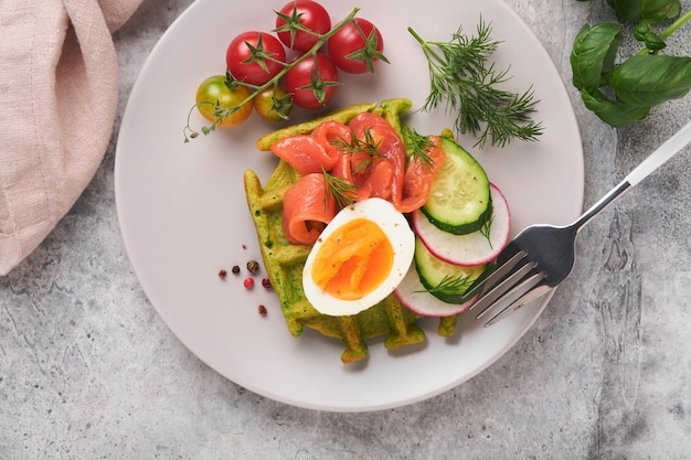 Savory waffles Breakfast green waffles wild garlic or spinach with egg tomato salmon on plate for breakfast on grey concrete table background Light dinner lunch or breakfast Top view Mock up