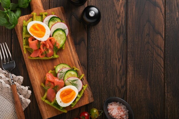 Cialde salate colazione cialde verdi aglio selvatico o spinaci con uovo pomodoro salmone su piatto di legno per colazione su vecchio sfondo di legno scuro cena leggera pranzo o colazione vista dall'alto mock up