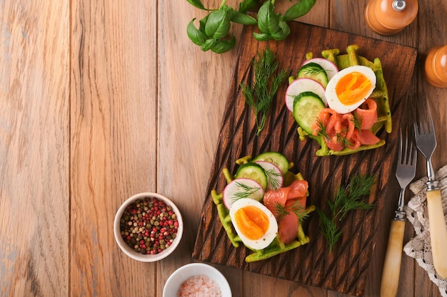 Savory waffles Breakfast green waffles wild garlic or spinach with egg tomato salmon on wooden plate for breakfast on old wooden background Light dinner lunch or breakfast Top view Mock up