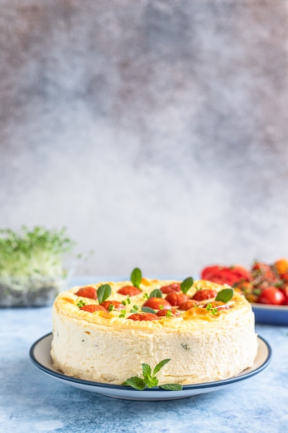 Savoury cheesecake with tomatoes decorated with mint, blue concrete background. Selective focus.