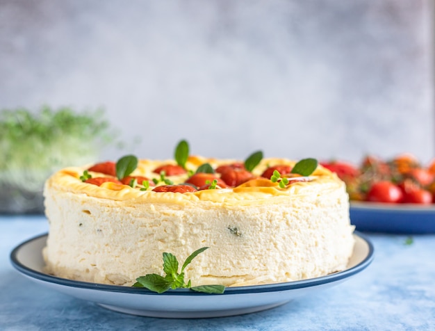 Cheesecake salata con pomodori decorati alla menta, fondo cemento blu.