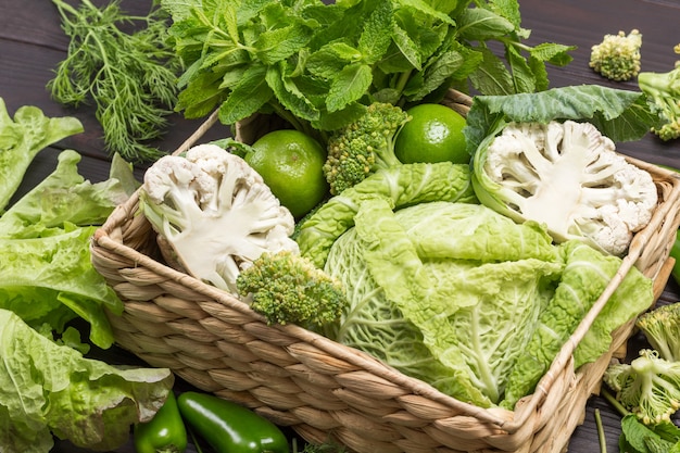 Savoy cabbage, broccoli and cauliflower in rattan basket. Wooden background. Top view