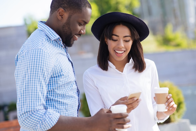 Savvy young pretty woman using her smartphone for showing pictures while telling exciting stories during the date