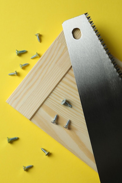 Saw, screws and wooden board on yellow background