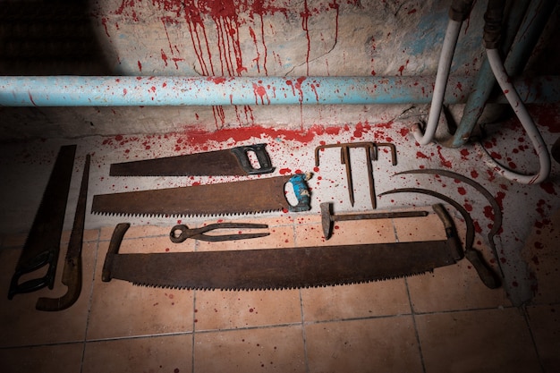 Photo saws, tongs and other devices on the bloody floor  in basement with pipes and wires in a halloween horror concept