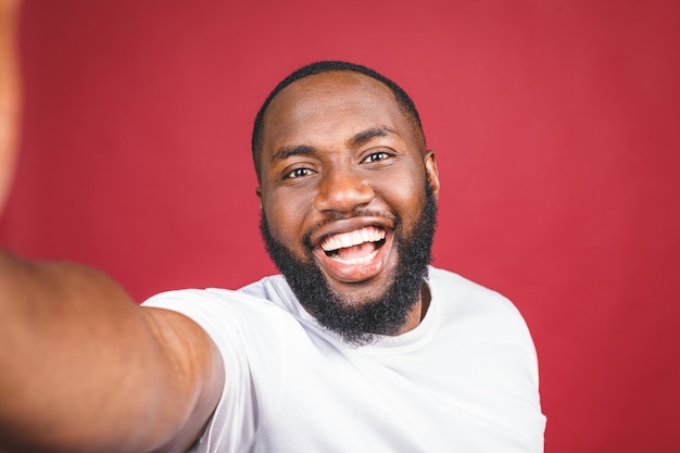 Say cheese. close up of young beautiful dark-skinned black man in casual smiling with teeth, holding smartphone, making selfie photo.