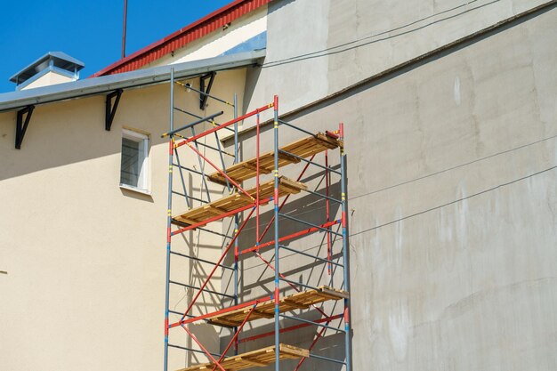 Scaffolding is installed along the wall of the building under construction Plastering and painting of the facade of the house Metal supports and wooden platforms for working at height