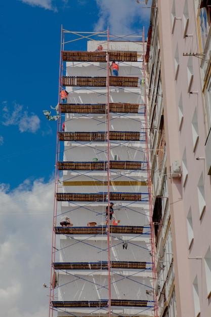 Scaffolding on a multistory building Warming of the outer wall panel A working man isolates the walls of a multistory building