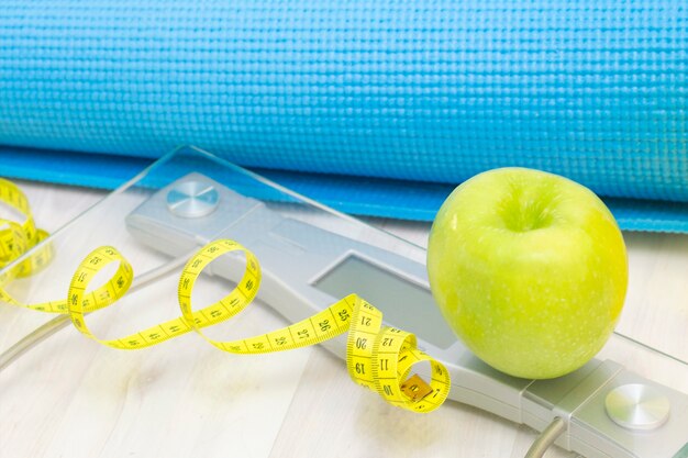 Весы, зеленое яблоко, рулетка, бутылка с водой и спортивные маты на светлой деревянной поверхности. потеря веса и спортивная концепция