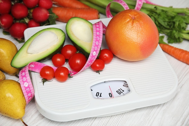scales healthy food and measuring tape on white wooden table