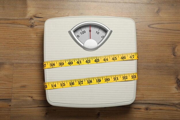 Scales tied with measuring tape on wooden background top view