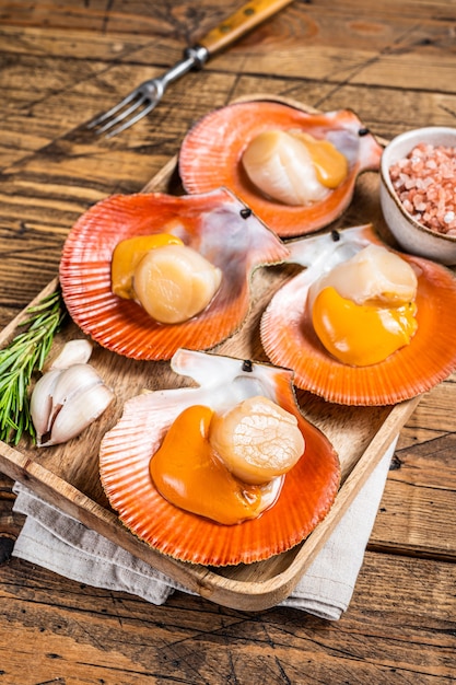 Scallops seafood on a wooden board with salt and herbs. wooden background. Top view.