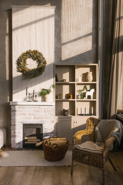 Scandinavian interior of a country house A living room with a fireplace and a wicker armchair with a plaid by the window decorated for Christmas Shelves with vases and candles