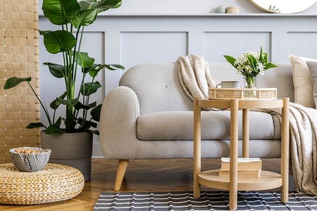 디자인 회색 소파, 목재 커피 테이블, 열대 식물, 선반, 거울, 가구, 격자 무늬 베개, 주전자, 책 및 가정 장식의 우아한 개인 액세서리가있는 스칸디나비아 거실 인테리어.