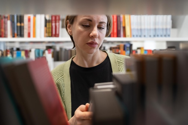 Scandinavian middleaged woman choosing textbook looking for literature while preparing for exam