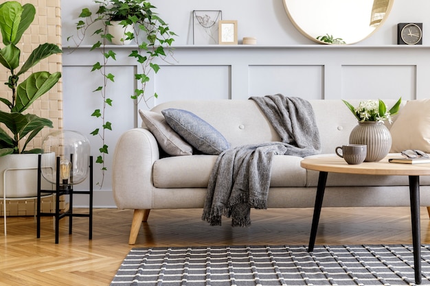 Scandinavisch concept van woonkamerinterieur met designbank, salontafel, plant in pot, bloemen, tapijt, plaid, kussen, plank, decoratie en persoonlijke accessoires in moderne huisinrichting.