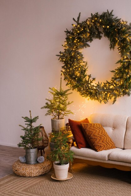 Scandinavisch interieur van de woonkamer met een gezellige bank met kussens en een kerstkrans op de muur kleine kerstbomen in potten