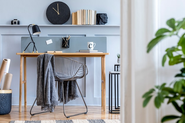 Scandinavisch kantoor aan huis interieur met houten bureau, design stoel, houten lambrisering met plank, plant, tafellamp, tapijt, kantoorbenodigdheden en elegante accessoires in een moderne woondecoratie.