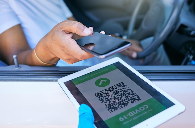 Photo scanning qr code to permit travel during covid lockdown at a checkpoint stop or border person holding phone to scan a corona passcode barcode or password on a tablet at a vaccination site