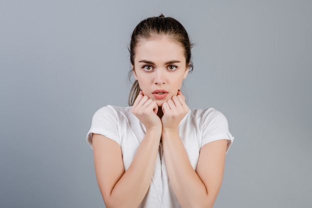 Scared anxious brunette woman holding fists close to her face isolated over grey