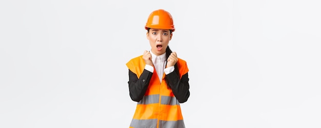 Scared asian female engineer in panic looking shocked and afraid shivering from fear wearing safety helmet and reflective jacket feel concerned and alarmed as having problem at construction zone