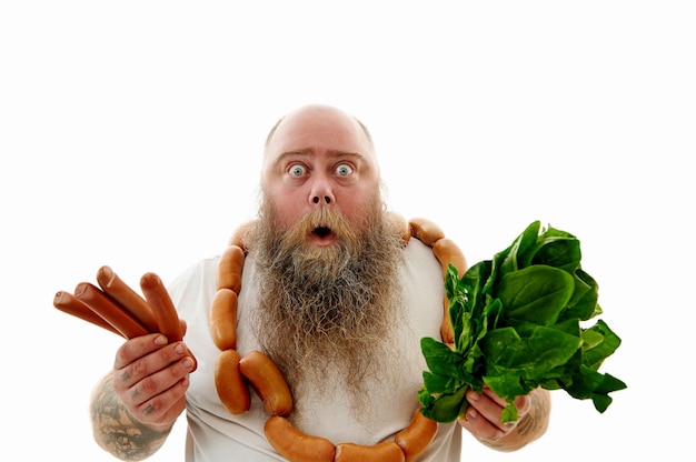 A scared bearded overweigt man wearing a bruch of sausages aroud the neck showing sausages and greens to the camera and expressing fear and surprise