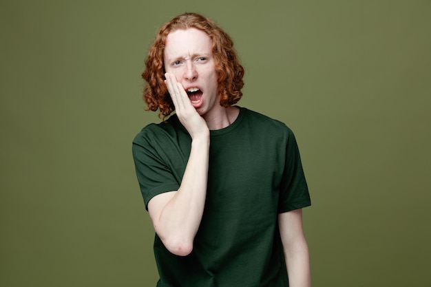 Scared covered face with hand young handsome guy wearing green t shirt isolated on green background