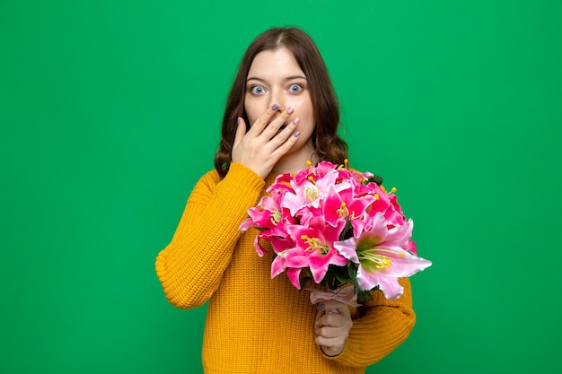 Scared covered mouth with hand beautiful young girl holding bouquet