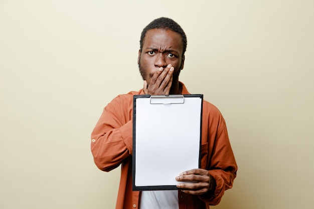 Scared covered mouth with hand young african american male holding clipboard isolated on white background