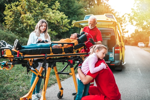 Scared girl standing next to her injured mother and doctors.