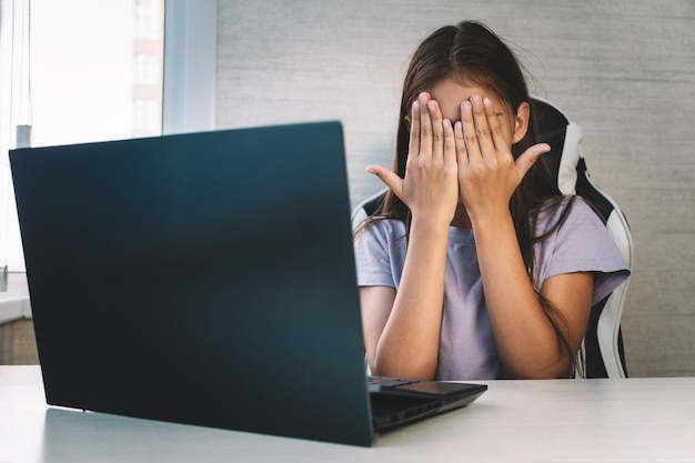 scared little girl closing face with hands looking at laptop screen prohibited information on Internet for children the concept of age censorship