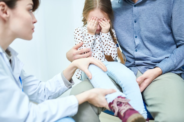 Bambina spaventata con gli occhi vicini a mano all'appuntamento del medico