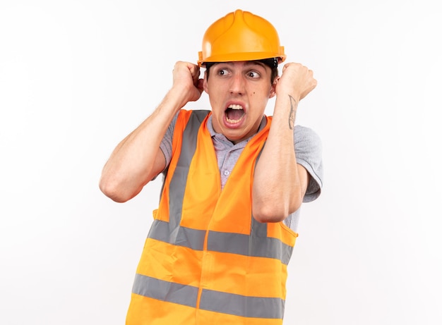 Scared looking side young builder man in uniform isolated on white wall