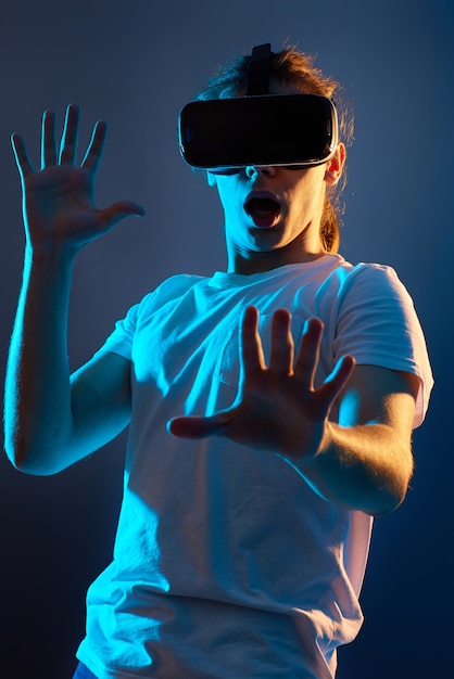 Scared man in glasses of virtual reality playing video games on\
dark blue background. neon light.