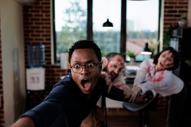 Photo scared man running from creepy zombies, trying to eat human brain in business startup office. bloodthirsty eerie monsters with wounds chasing after frightened scared person, angry corpses.