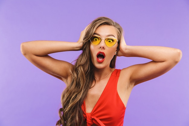 Фото Испуганная или шокированная женщина в красном платье и солнцезащитных очках кричит и закрывает уши руками