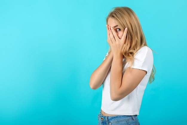 Photo scared pretty young woman hiding behind hands, peeping through fingers, curious funny female