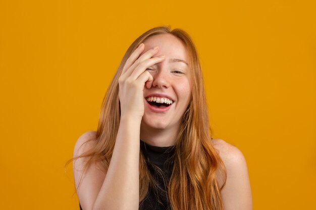 Giovane donna dai capelli rossi spaventata isolata sul nascondiglio giallo della parete dietro le mani, fronte spaventato della copertura della ragazza della testarossa che sbircia guardando attraverso le dita, sbirciare spaventata di sensibilità femminile curiosa.