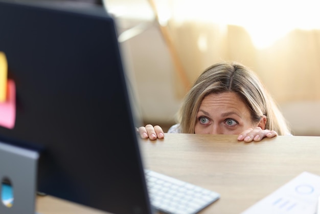 Scared and shocked woman in panic behind desk looking at computer screen getting bad news