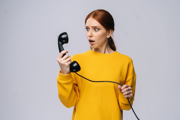 Фото Испуганная шокированная молодая женщина в стильном желтом свитере разговаривает по ретро-телефону