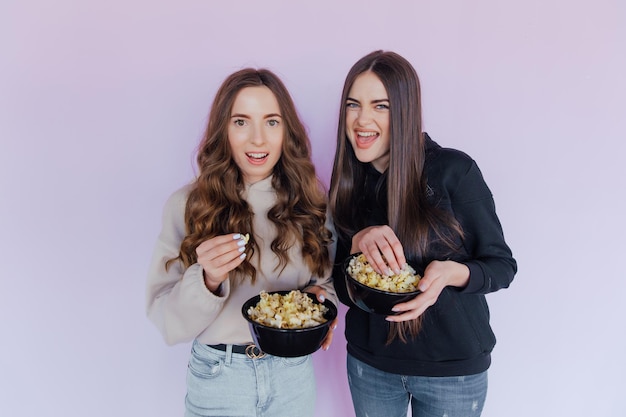 Scared shocked young women girls friends watching movie film hold bucket of popcorn