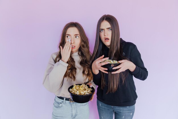 Scared shocked young women girls friends watching movie film hold bucket of popcorn