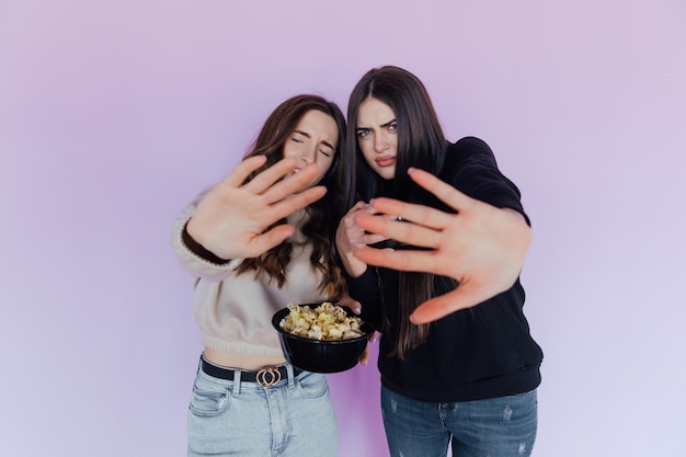 Scared shocked young women girls friends watching movie film hold bucket of popcorn