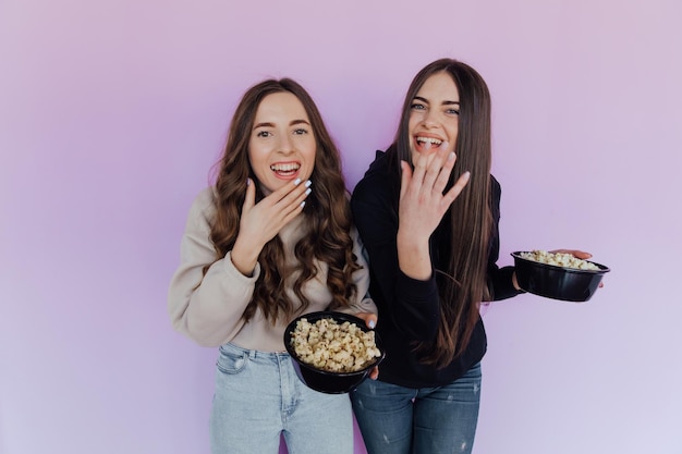 Scared shocked young women girls friends watching movie film hold bucket of popcorn