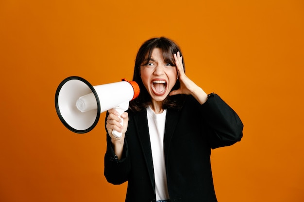 Scared speaks on loudspeaker young beautiful female wearing black jacket isolated on orange background