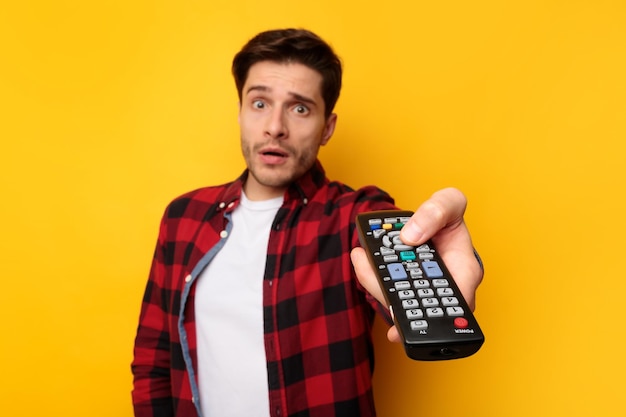 Scared young guy watching tv holding remote control